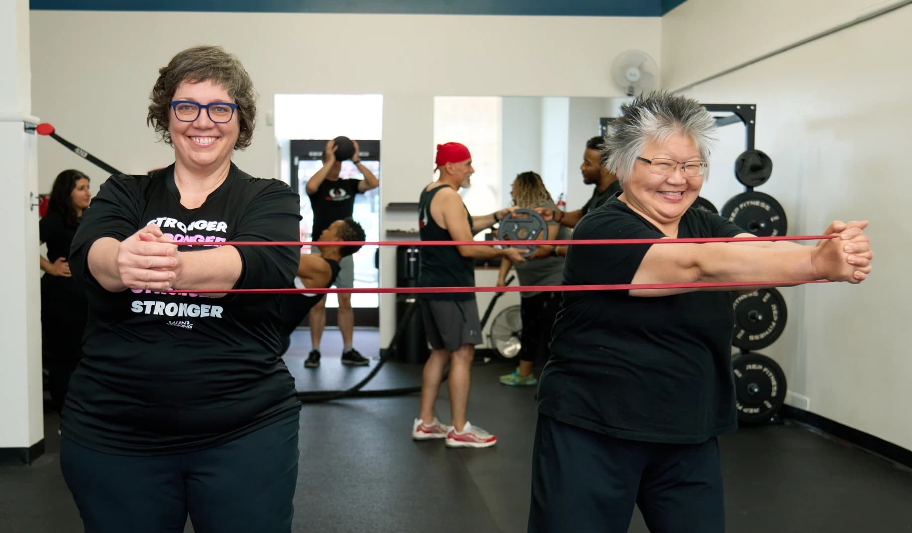 Two members hold a resistance band between them while others train behind them in the studio.