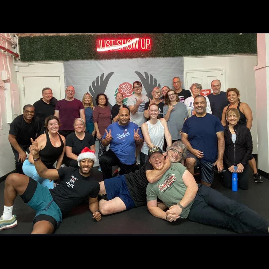 Members and coaches posing together under the Just Show Up wings mural in the studio.