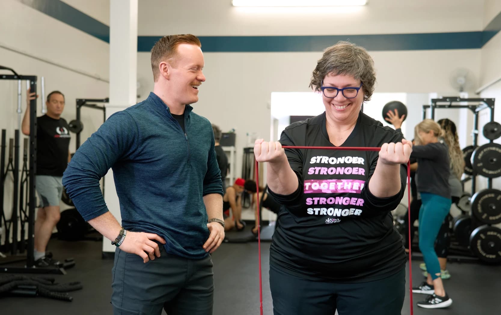 A coach stands alongside a member as she pulls a resistance band during her session.