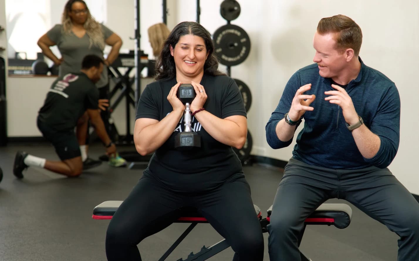 A coach talks a member through a squat while she holds a dumbbell at her chest.